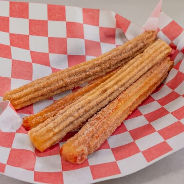 Four golden-brown churros, coated in cinnamon sugar, rest on red and white checkered paper.
