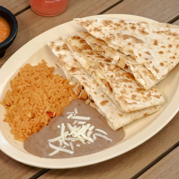 A plate of quesadillas with rice and refried beans, topped with shredded cheese, on a wooden table.