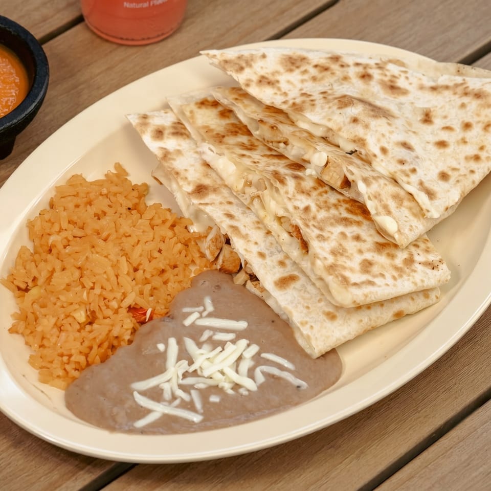 A plate of quesadillas, rice, and refried beans with shredded cheese on a wooden table.